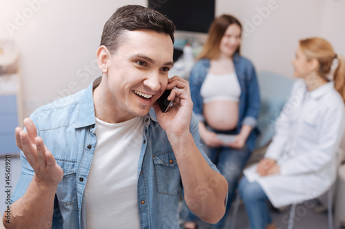 Fotografie, Obraz Positive future father sharing news with relatives in the clinic