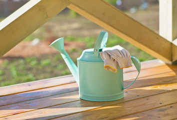 Watering can and garden gloves on spring garden background