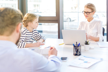 businesswoman working with laptop, businessman reading newspaper and daughter drawing near in office