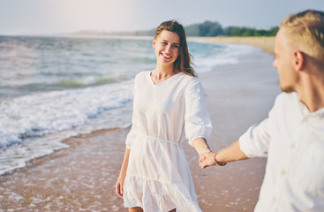 Wall Mural - Romantic dating. Young loving couple walking together by the sand beach enjoying sea