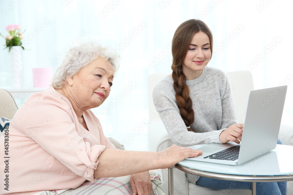 Beautiful girl with grandmother using laptop at home