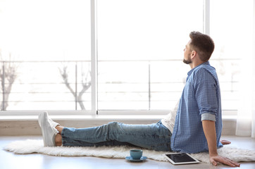 Wall Mural - Happy young man sitting on floor near window