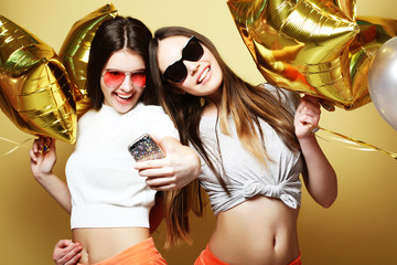 Two teenage girls friends with gold balloons  make selfie on a p