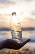 Female hand with a plastic bottle of water on a sky background	