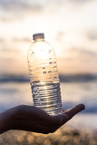 Fototapeta Desenie - Female hand with a plastic bottle of water on a sky background	