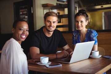 Wall Mural - Portrait of friends using laptop while having coffee