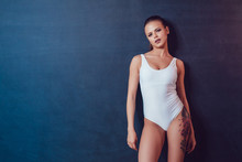 Beautiful Sexy Girl With Tattoo In White Bodysuit Standing On A Black Background. Mock Up.