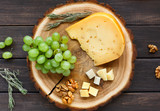Fototapeta  - Cheese platter, gouda herb on natural wood disc with grapes and nuts