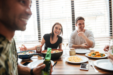 Sticker - Multiracial young friends enjoying meal while sitting at the dinning table