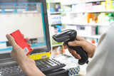 Fototapeta Desenie - Pharmacist scanning price on a red medicine box with barcode reader in pharmacy store