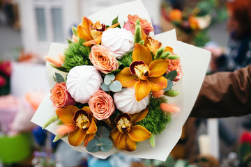 Original unusual edible bouquet of marshmallow and fresh orchids, roses. Close up. Selective focus. Flower delivery. Bunch of flowers in men's hand