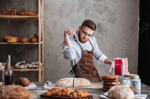 Fotomural Concentrated man baker standing at bakery near bread
