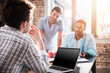 © LIGHTFIELD STUDIOS - Young man using laptop while colleagues discussing project, small business meeting concept