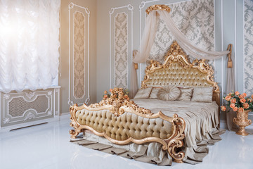 Luxury bedroom in light colors with golden furniture details. Big comfortable double royal bed in elegant classic interior