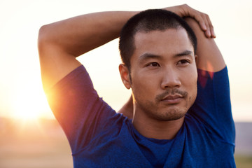 Wall Mural - Focused young Asian man stretching his shoulders before a run