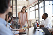 © Monkey Business - Young woman stands addressing colleagues at business meeting