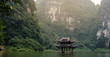 A scene of wooden bell tower floating on the water, surrounded by cliffs and jungle