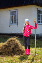 Adorable 8 Years Old Girl Running With Rake In The Country In Early Spring, Garden, Rake The Dry Grass, The Concept Of Helping And Working Children In The Country