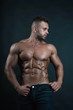 © zoya - Handsome muscular well-shaped tanned sexy bodybuilder/male fitness model with tattoo and perfect abs poses over dark background looking to his left in natural colors