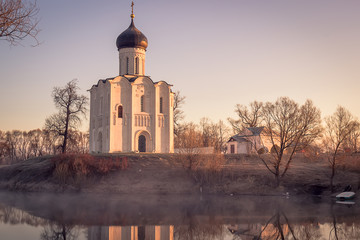 A misty lake with a boat in front of the church in the early spring at dawn