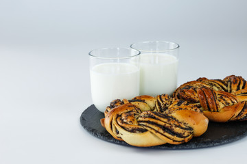 Baked pastry with poppy seeds on black plate with glass of milk with white background