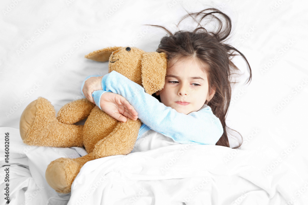 Cute little girl lying in bed with cuddly toy