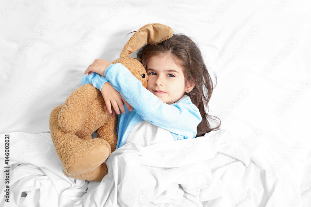 Cute little girl lying in bed with cuddly toy