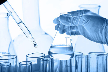 Wall Mural - flask in scientist hand with lab glassware background