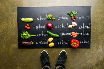 Wall Mural - partial view of man standing near fresh vegetables and calories table, healthy lifestyle concept