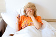 Kobieta blondynka w łóżku zakrywająca dłonią twarz.