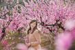 © TwinkleStudio - Cute beautiful stylish dressed brunette girl with mother mom standing on a field of spring young peach tree with pink flowers.Lady dressed in rain clothes and blue hat rubber boots spring season.