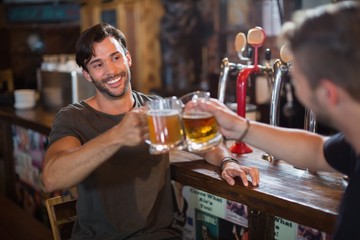 Smiling man toasting beer mug with male friend