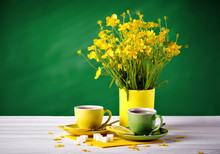 Two Cups With Tea And Lemon Are On The Wooden Table. Vase With Yellow Buttercups On A Green Background.
