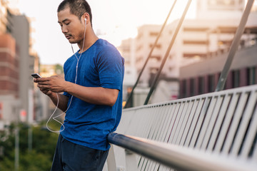 Canvas Print - Sporty Asian man choosing music before a run