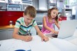 © WavebreakMediaMicro - Boy doing his homework while girl using laptop in kitchen