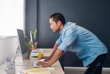 Young Asian designer standing at his desk using a computer