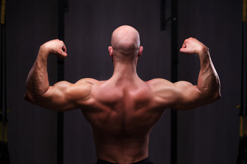 Wall Mural - Young healthy bald ripped man with big muscles posing in gym, view from the back