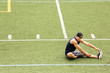 Young man stretching leg while sitting on sports field 
