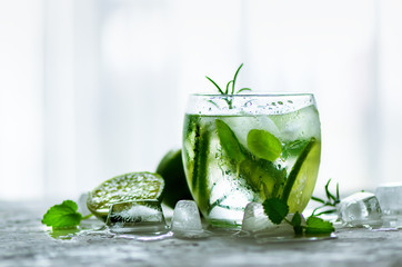 Wall Mural - Homemade lime lemonade with cucumber, rosemary and ice, white background. Cold beverage for hot summer day. Copyspace.