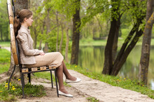 Beautiful Young Woman Sitting On Bench In Park Looking Ahead