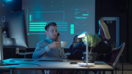Bored man developer in office drinking coffee and working with laptop close notebook and put his hands on table
