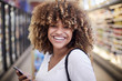 © Granger Wootz/Blend Images - Black woman holding cell phone smiling in grocery store