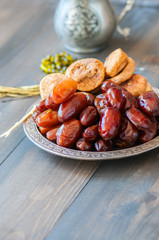 Close up of dried date fruits or kurma and figs served on a old vintage plate with ornaments and beads on a wooden background, ramadan food concept.