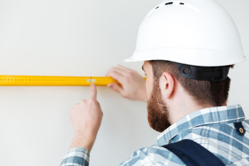 Back view of man builder using ruler to measure length