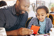 © Inti St Clair/Blend Images - Father and daughter sitting at restaurant table texting on cell phone