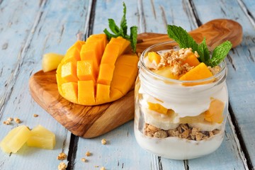 Wall Mural - tropical mango and pineapple parfait in a mason jar on a rustic blue wood background