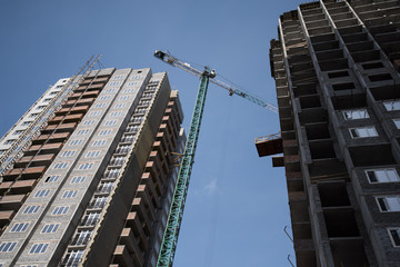 Crane and building construction site against blue sky. The erection of a new building. Streaming urbanization.