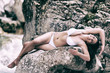 Vollbusige junge Frau liegt in weißen Dessous auf einen Felsen an einem rauschenden Gebirgsbach.