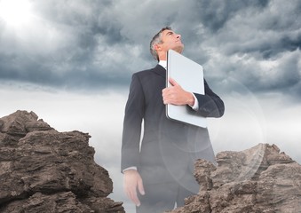 Wall Mural - Business man with laptop and flare looking up behind rocks