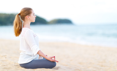 Wall Mural - woman practices yoga and meditates in lotus position on beach.